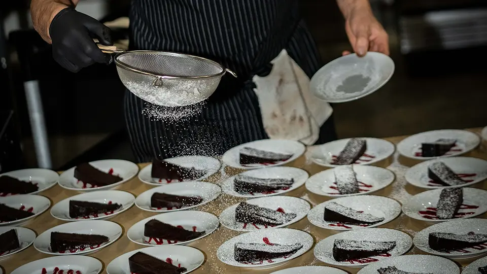 A picture of a chef preparing cake slices for a large crowd